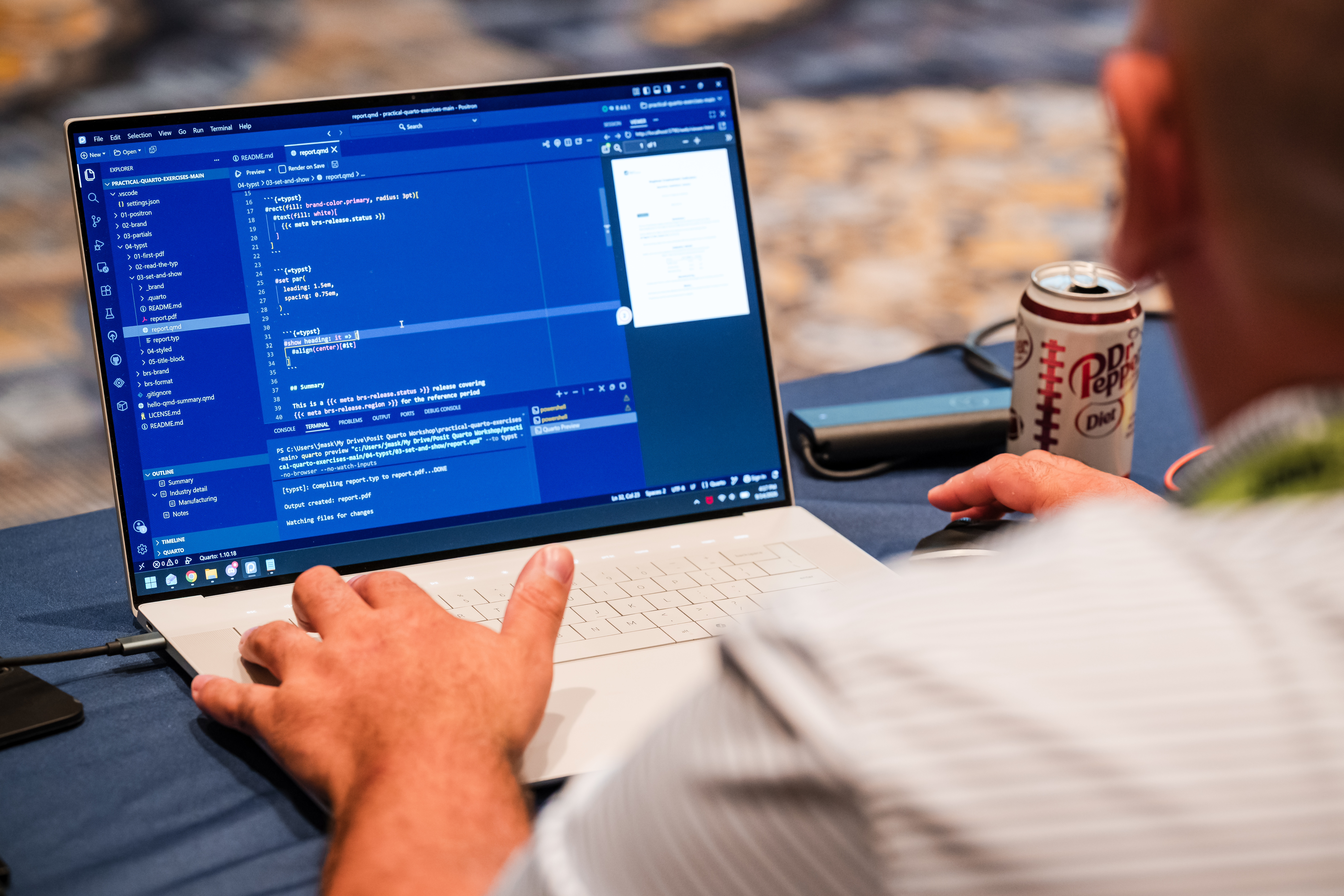 Over-the-shoulder view of a person using a laptop to edit code in a dark-themed code editor, with a can of Diet Dr Pepper on the table next to them.