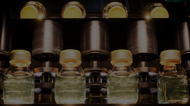 A close-up, high-angle shot of several small glass vials with yellow caps moving through an automated industrial assembly line