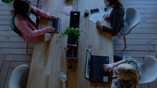 A photo from above of a table in a shared workspace with three women working on laptops