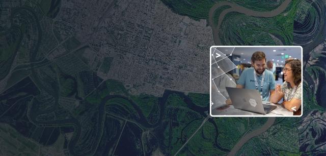 A dark blue-tinted satellite map background with a bright inset photo showing two colleagues collaborating over a laptop.