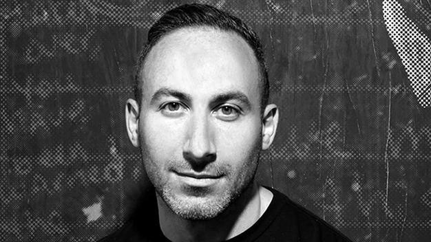 black and white portrait of Adam Bly standing in front of chalkboard with writing
