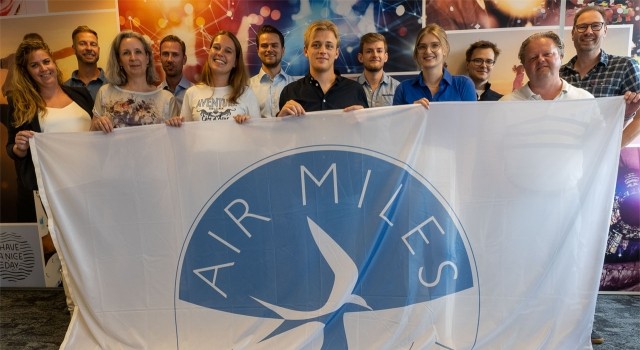 The airmiles team posing with a flag of their logo.
