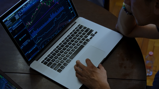 A person's hand on a laptop trackpad while analyzing complex financial data charts and graphs on a dark-mode dashboard.