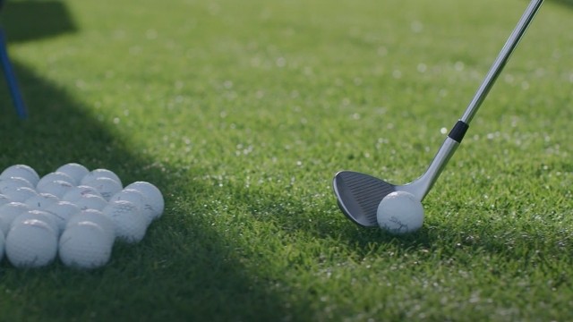 A golf club with a ball teed up and ready to hit, with a pile of balls to the side