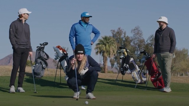A woman crouching down to see her line of put on a golf course with three male golfers standing behind her