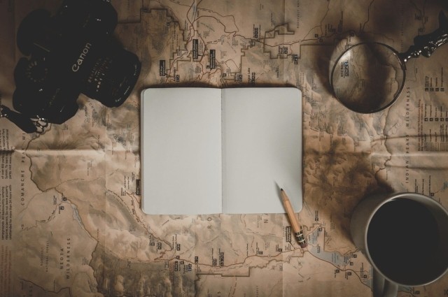 a journal, a pencil, and a coffee on top of a map