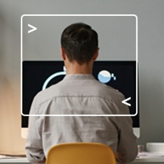 back view of a man sitting at desk working on computer with computer terminal framing him