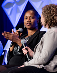 Two women with microphones speaking on a panel on stage at an event