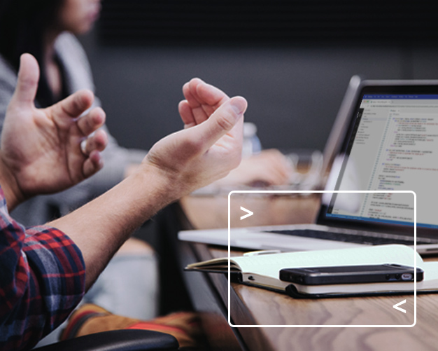 Man gesturing with hands while talking in conference room with a laptop, notebook and phone on the table