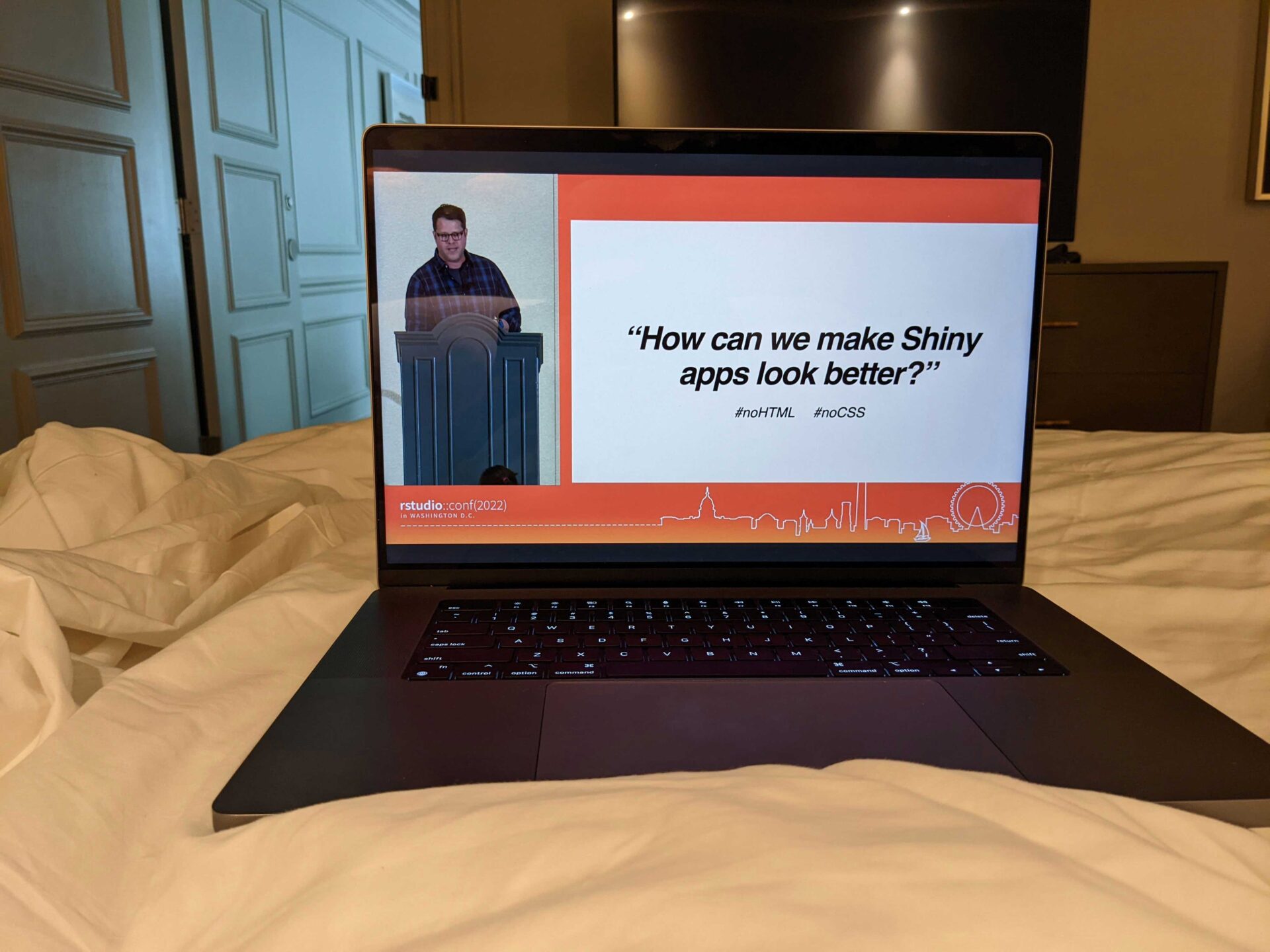 Text: How can we make Shiny apps look better? virtual conf2022 talk on laptop on bed