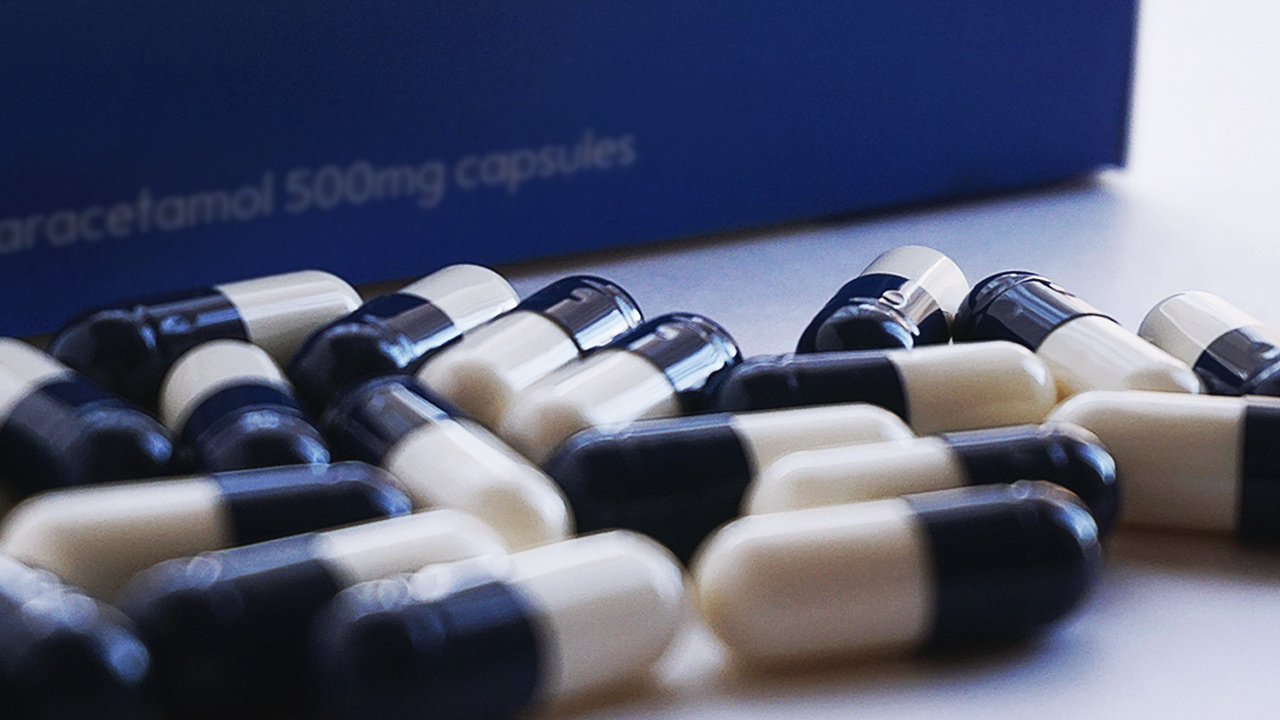 close up of blue and white pills next to a box with blurred text