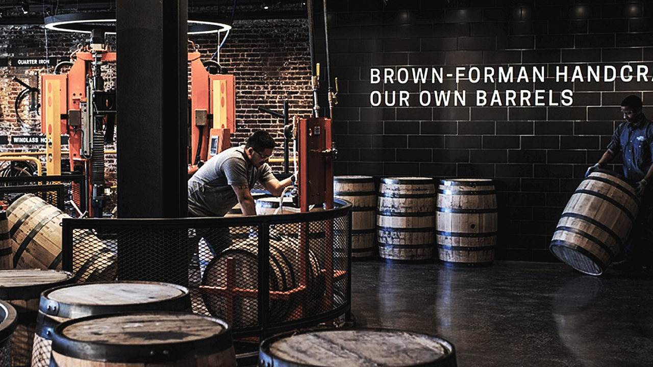 workers check and move barrels at a distillery under sign with Brown-Forman Handcr...Our Own Barrels texts