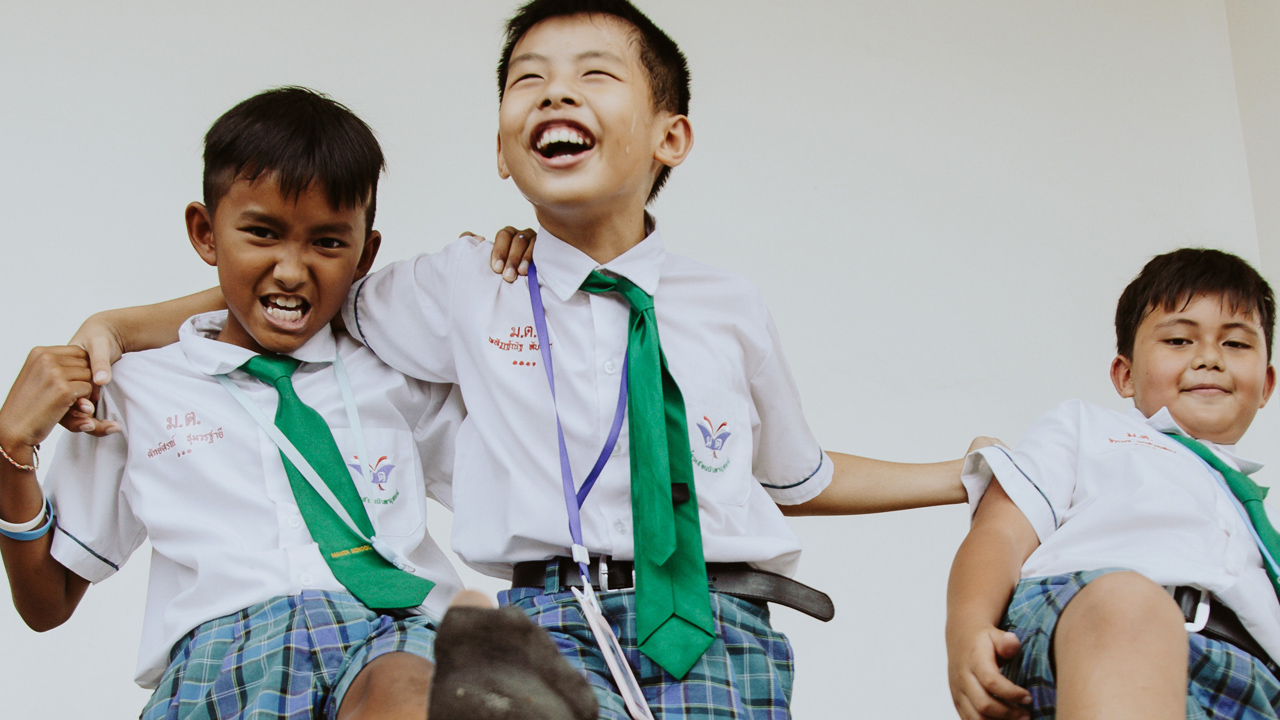 3 smiling, young boys from Thailand wearing school uniforms and playing
