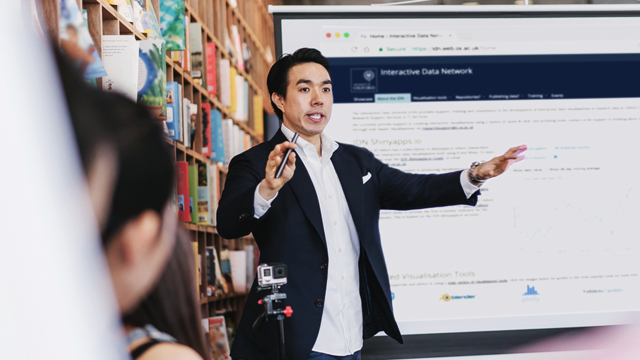 A man giving a presentation to a group in a library or college setting