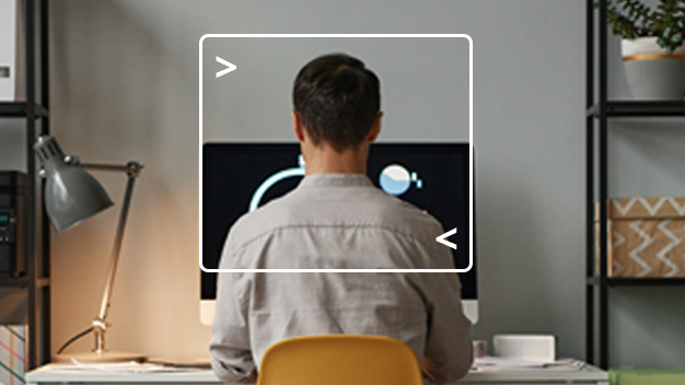 back view of a man sitting at desk working on computer with computer terminal framing him