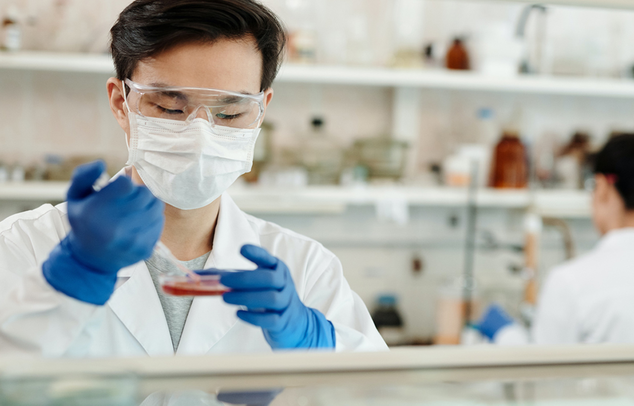scientist in a lab looking at a biological culture, another person out of focus in background