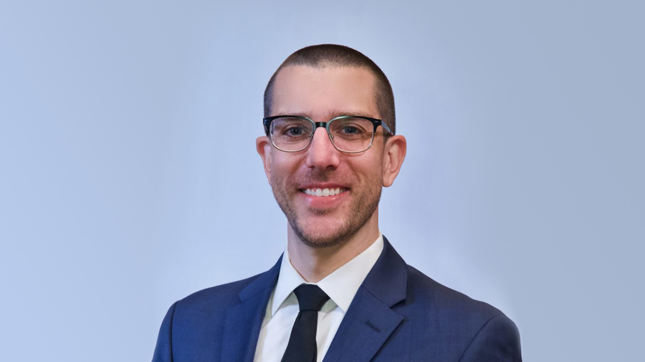 portrait of Justin Elszasz in front of solid light blue background