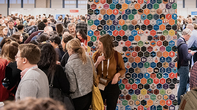 wall of hex stickers with large amount of people around it milling about at a past conference event