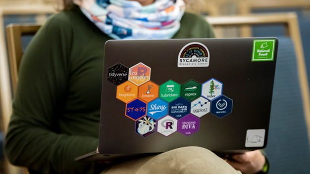 image of person from the neck down at a laptop with back of laptop full of hex stickers