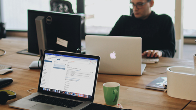 man sitting at large desks pushed together looking at two computer screens, a laptop open on the other side with Posit Package Manager UI