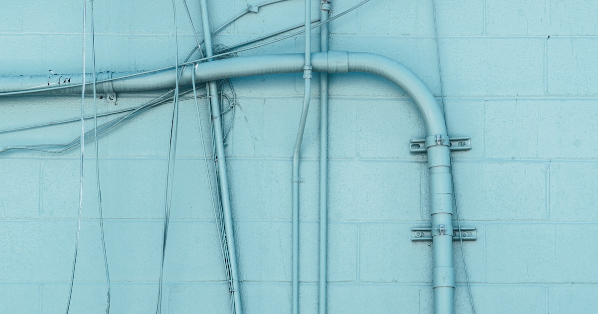 Pipes and wires on an external wall painted light blue to match the cement wall