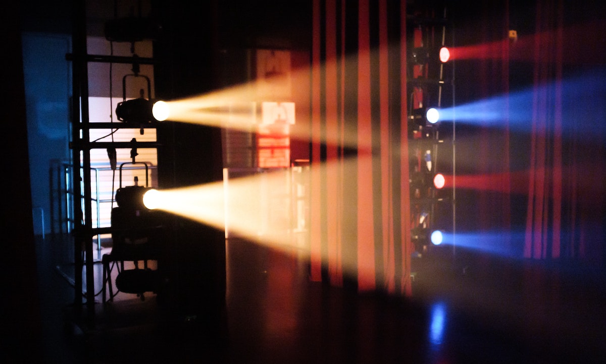 Spotlights on side booms with red and blue colour gels illuminating the backstage of a stage, smoke/haze around the lights.