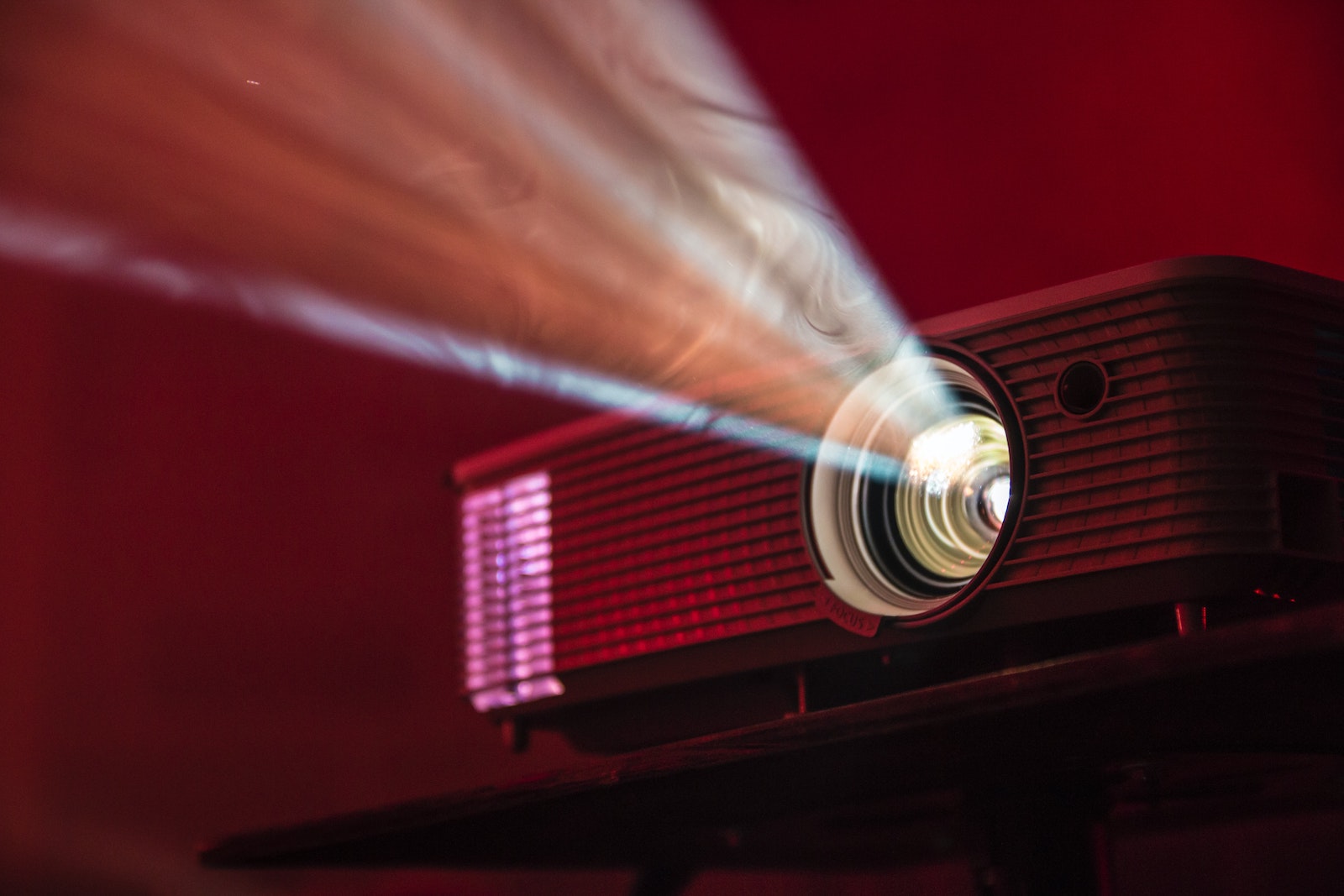 Close up of a projector in a red-lit room turned on revealing smoke in the light