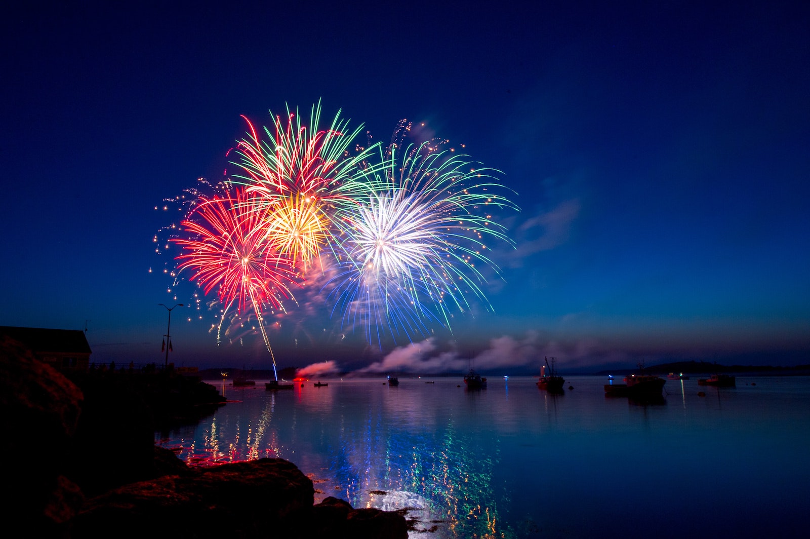 fireworks display at night over water with boats in the background and fireworks reflecting on the water