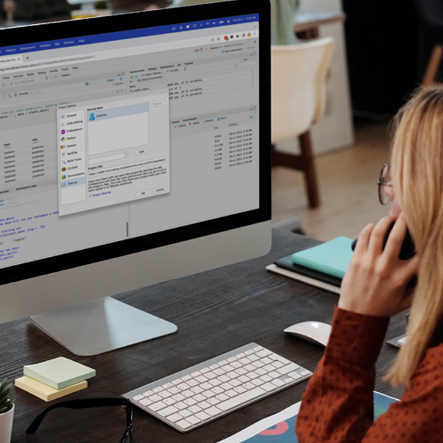 woman at desk looking at desktop computer with Posit Workbench screen and talking on phone