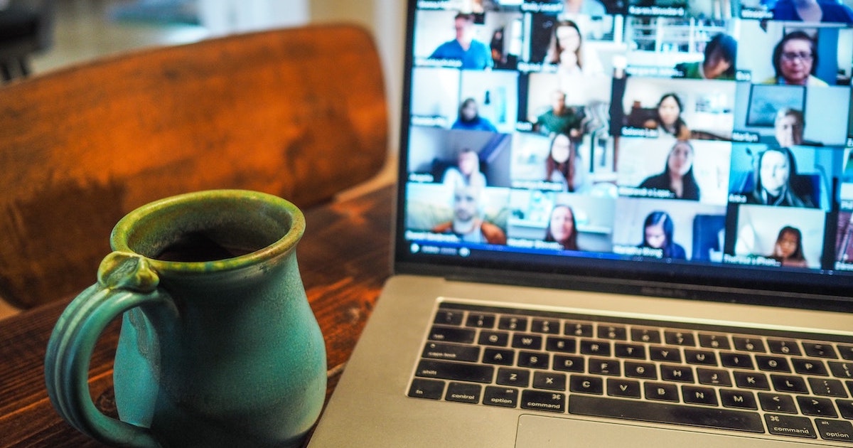 Coffee mug next to laptop with a blurred out Zoom screen with multiple people.