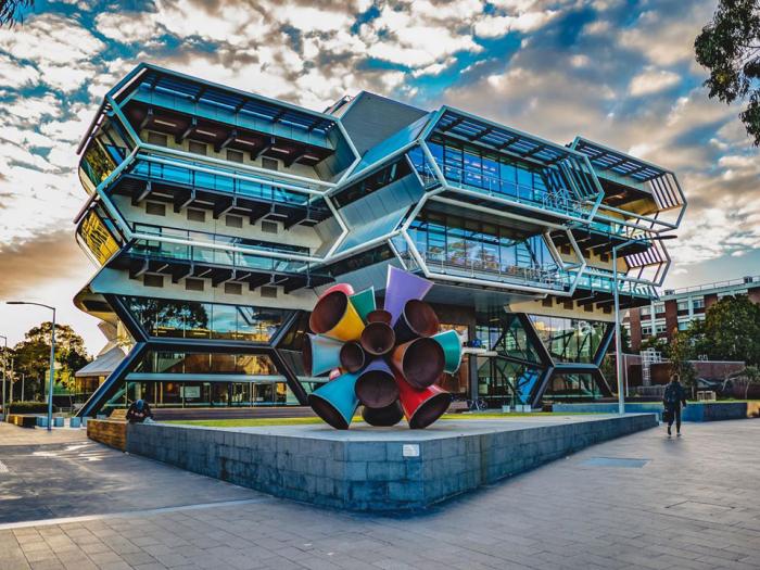 A colorful metal sculpture in fron of a modern building with 2 hexagonal floors