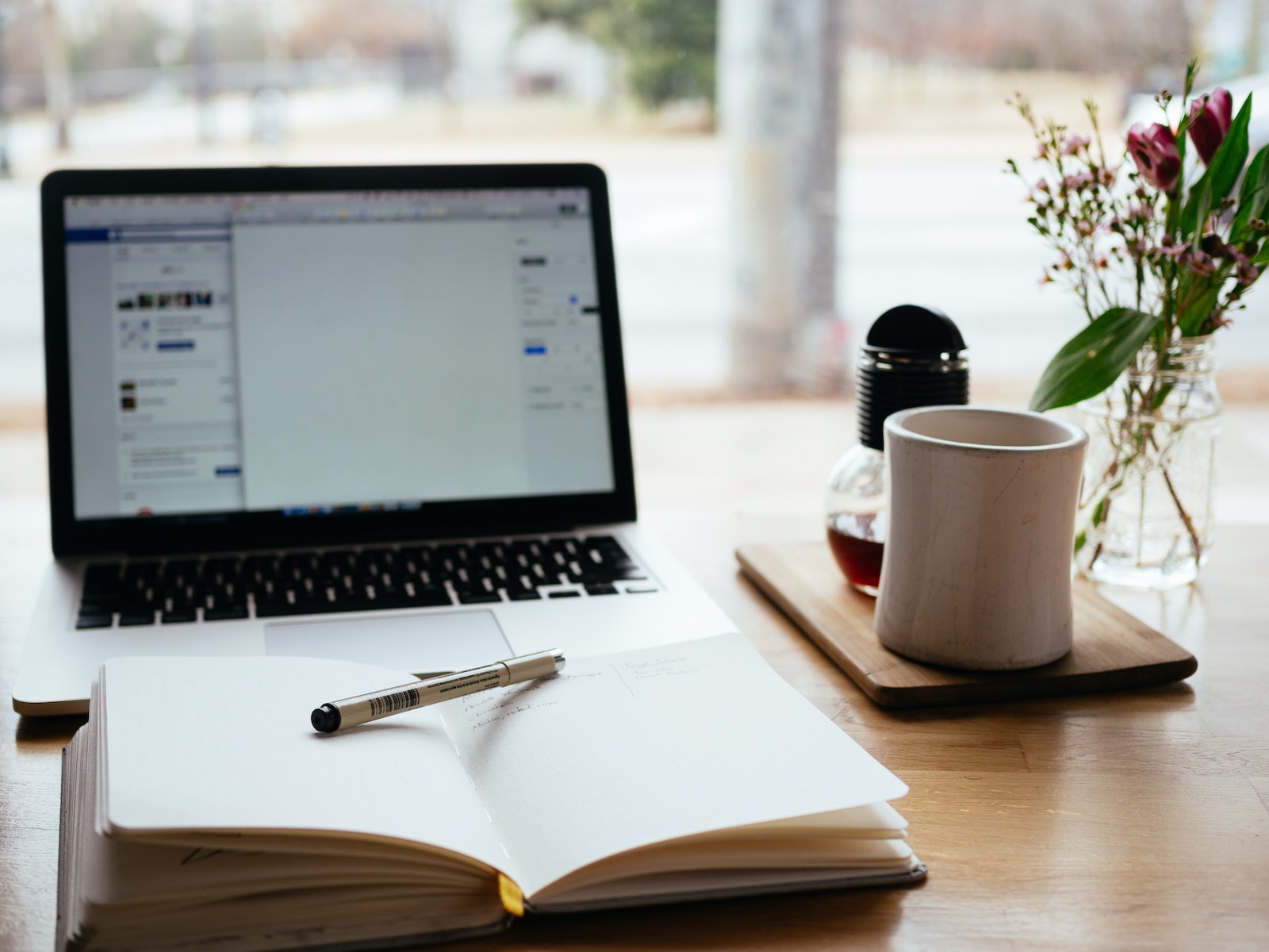 Open laptop and a notebook, a coffee mug, and flowers