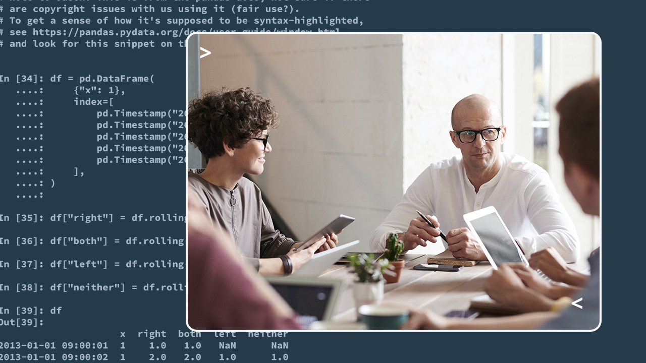 Three people at a table, looking like they're working and chatting. In the background is Python code.